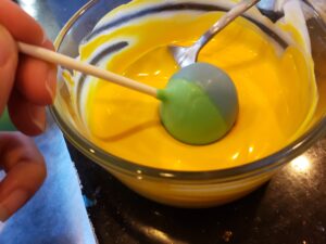 Jack Skeleton Cake Pops dipping the multi colored cake pop into the yellow candy melts