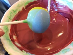 Jack Skeleton Cake Pops dipping the multi colored cake pop into the red candy melts